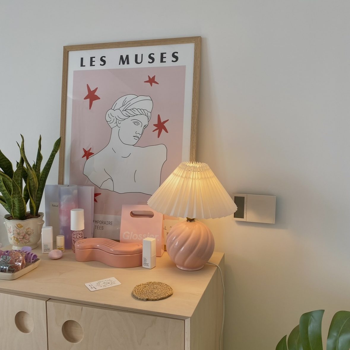 Light wood sideboard with vintage pink lamp on top.