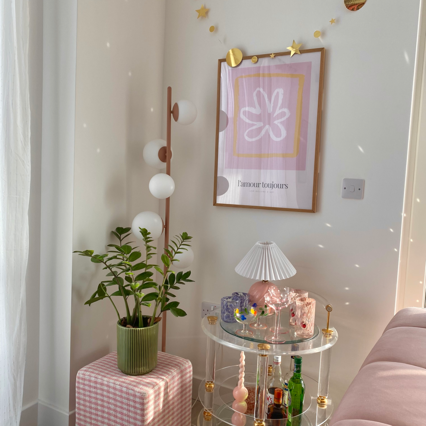 Corner of a pastel-inspired apartment that features a mini bar cart and plant placed on a gingham stool.